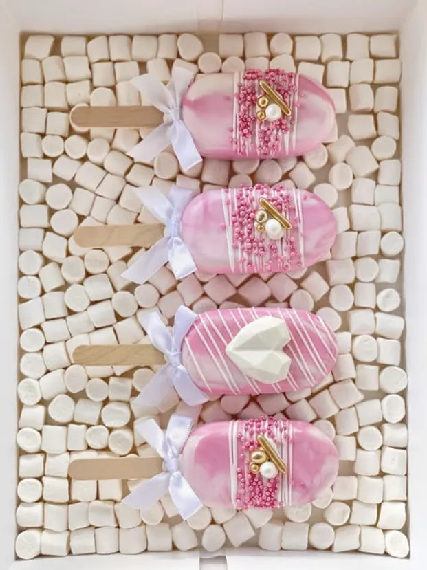 Fire rosa cakesicles med hvite sløyfer, perler og drizzle på marshmallows