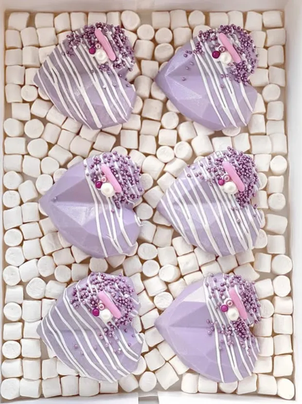 Fasetterte lilla cakehearts med hvit drizzle og perler i en eske fylt med marshmallows